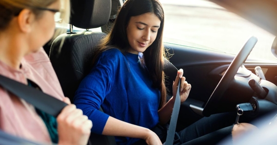 two women in front seat of a car, buckling their seatbelts